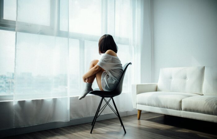 woman sitting on black chair in front of glass-panel window with white curtains