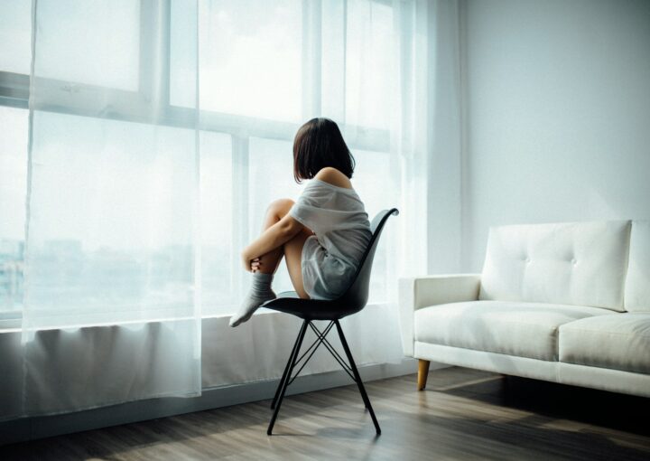 woman sitting on black chair in front of glass-panel window with white curtains