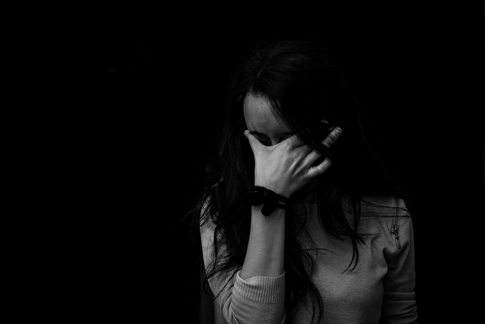 Intense black and white portrait capturing the emotion and introspection of a woman covering her face.