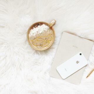 Minimalist flat lay of coffee, smartphone, notebook, and pen on white fur.