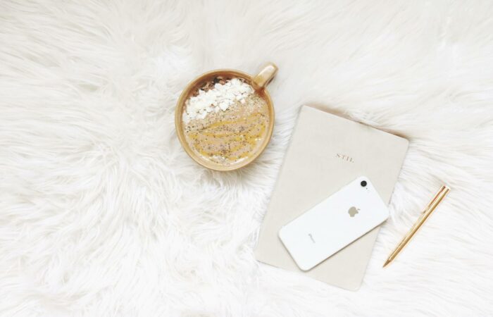 Minimalist flat lay of coffee, smartphone, notebook, and pen on white fur.