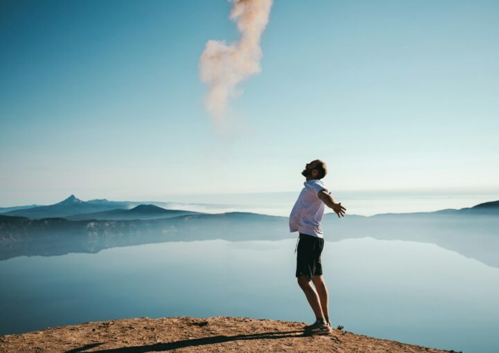 man standing on sand while spreading arms beside calm body of water