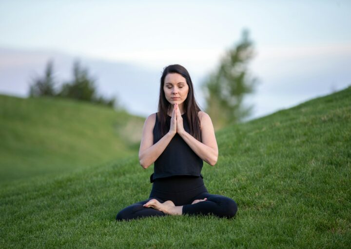 woman in black tank top and black pants sitting on green grass field during daytime