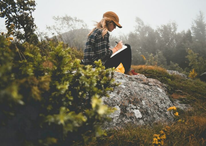 a woman sitting on top of a rock writing