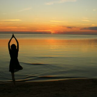woman doing yoga near calm body of water during golden hour