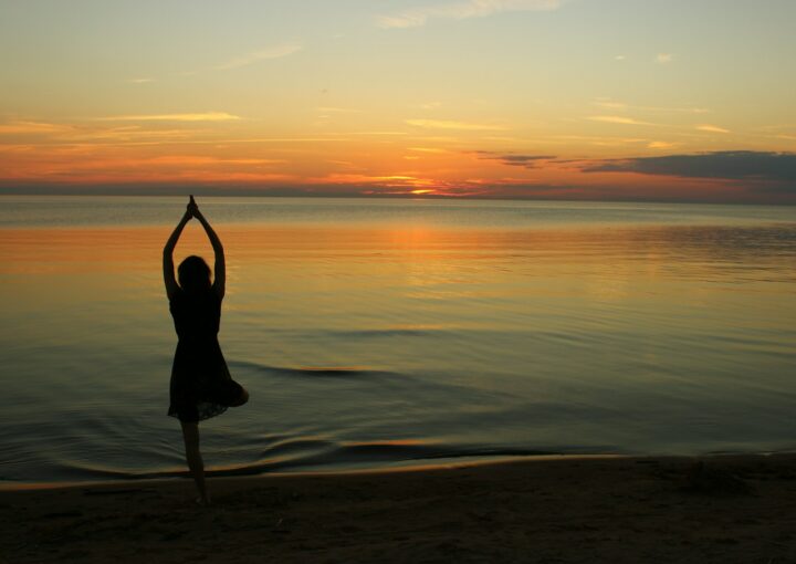 woman doing yoga near calm body of water during golden hour