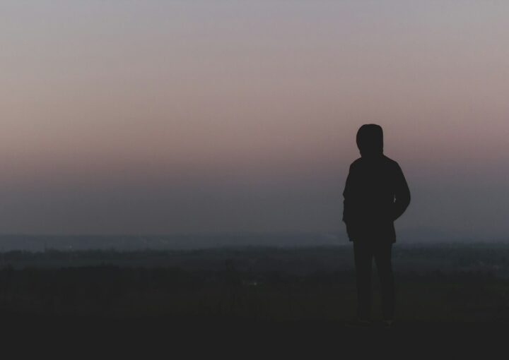 silhouette of man standing on hill during sunset