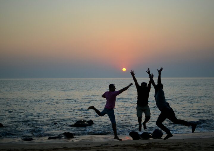 three people jumping on the beach at sunset