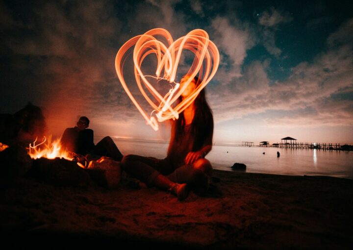 woman sitting on sand near bonfire