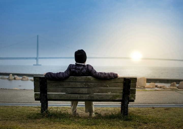 person sitting on bench facing suspension bridge