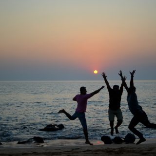 three people jumping on the beach at sunset