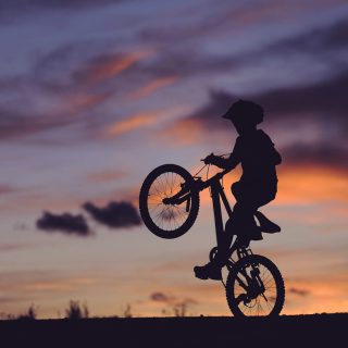 silhouette of boy riding bicycle in wheelie during golden hour