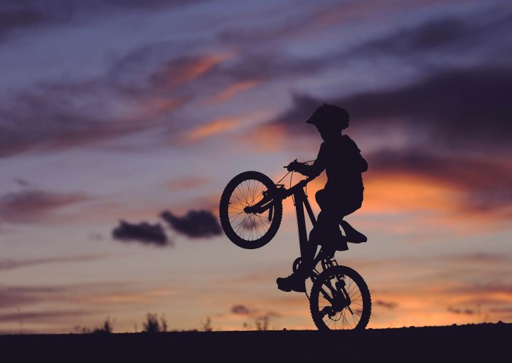 silhouette of boy riding bicycle in wheelie during golden hour