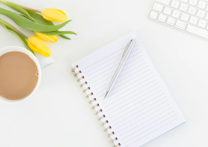 white notebook with yellow tulips beside white ceramic mug with coffee