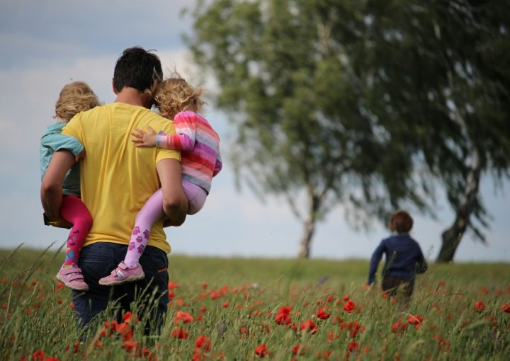 man carrying to girls on field of red petaled flower