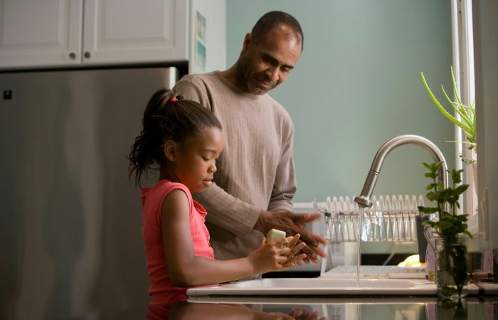 man in long sleeve shirt standing beside girl in pink tank top washing hands