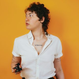 Portrait of a nonbinary autistic person in a studio setting with a stim toy in their hand