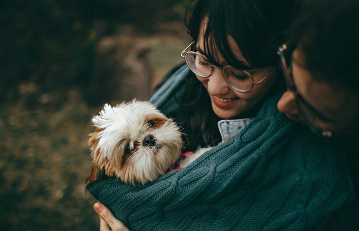 A woman lovingly cuddles her Shih Tzu puppy, wrapped in a warm blanket outdoors.