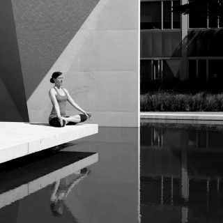 A woman meditating by a poolside, reflecting tranquility and focus in a minimalist setting.