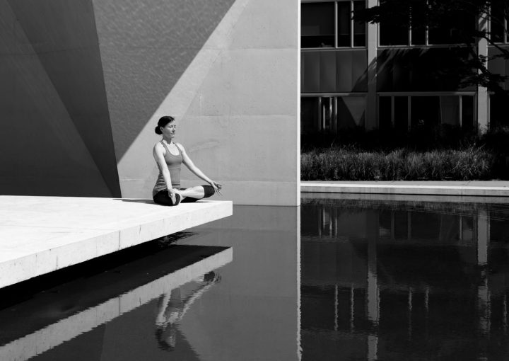A woman meditating by a poolside, reflecting tranquility and focus in a minimalist setting.