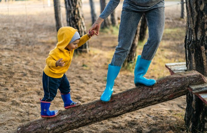 A woman helps her toddler walk on a log in a park, showcasing child support and family bonding.