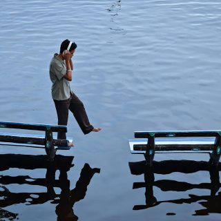 Young man balancing between two benches on water's surface, Amarapura, Myanmar.