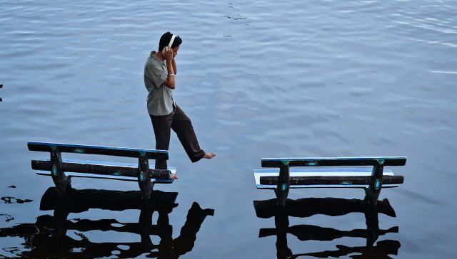 Young man balancing between two benches on water's surface, Amarapura, Myanmar.