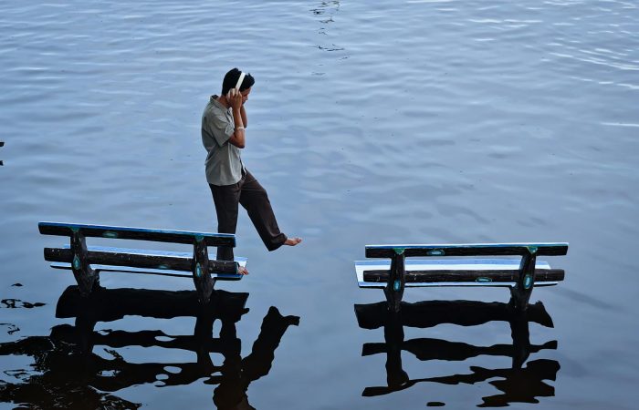 Young man balancing between two benches on water's surface, Amarapura, Myanmar.
