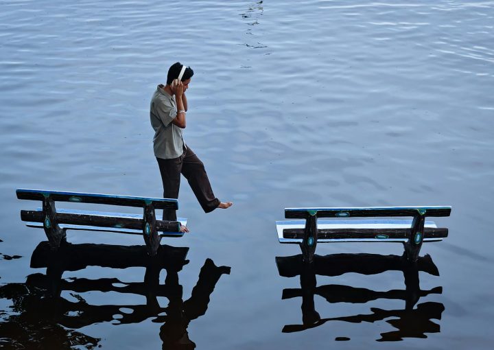Young man balancing between two benches on water's surface, Amarapura, Myanmar.