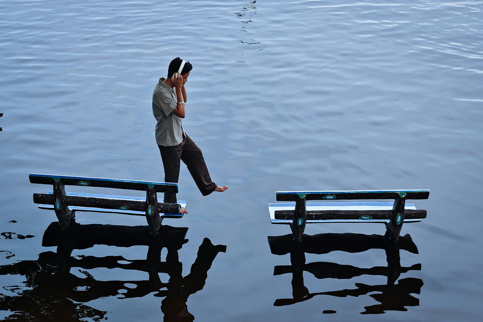 Young man balancing between two benches on water's surface, Amarapura, Myanmar.