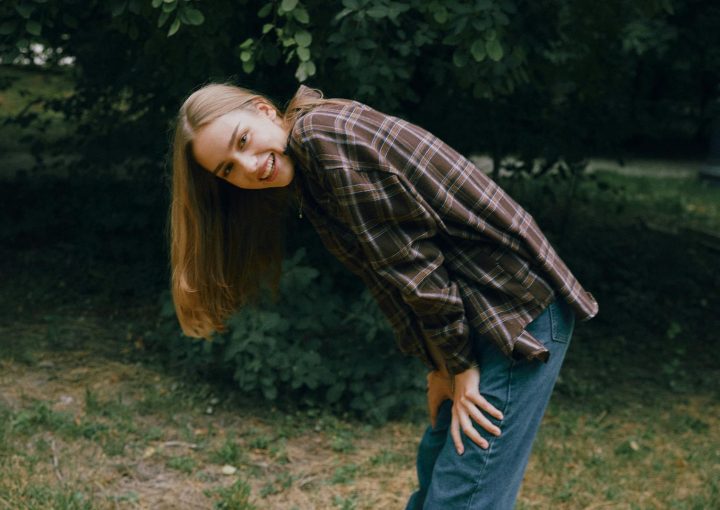 A joyful young woman with long hair bends and smiles outdoors in casual attire.