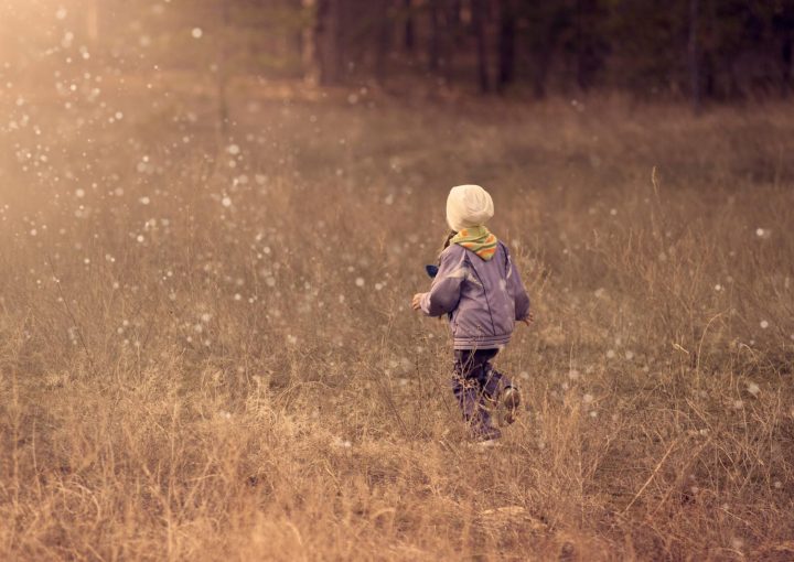 A young child runs through a grassy field during sunset, enjoying the freedom of outdoor play.