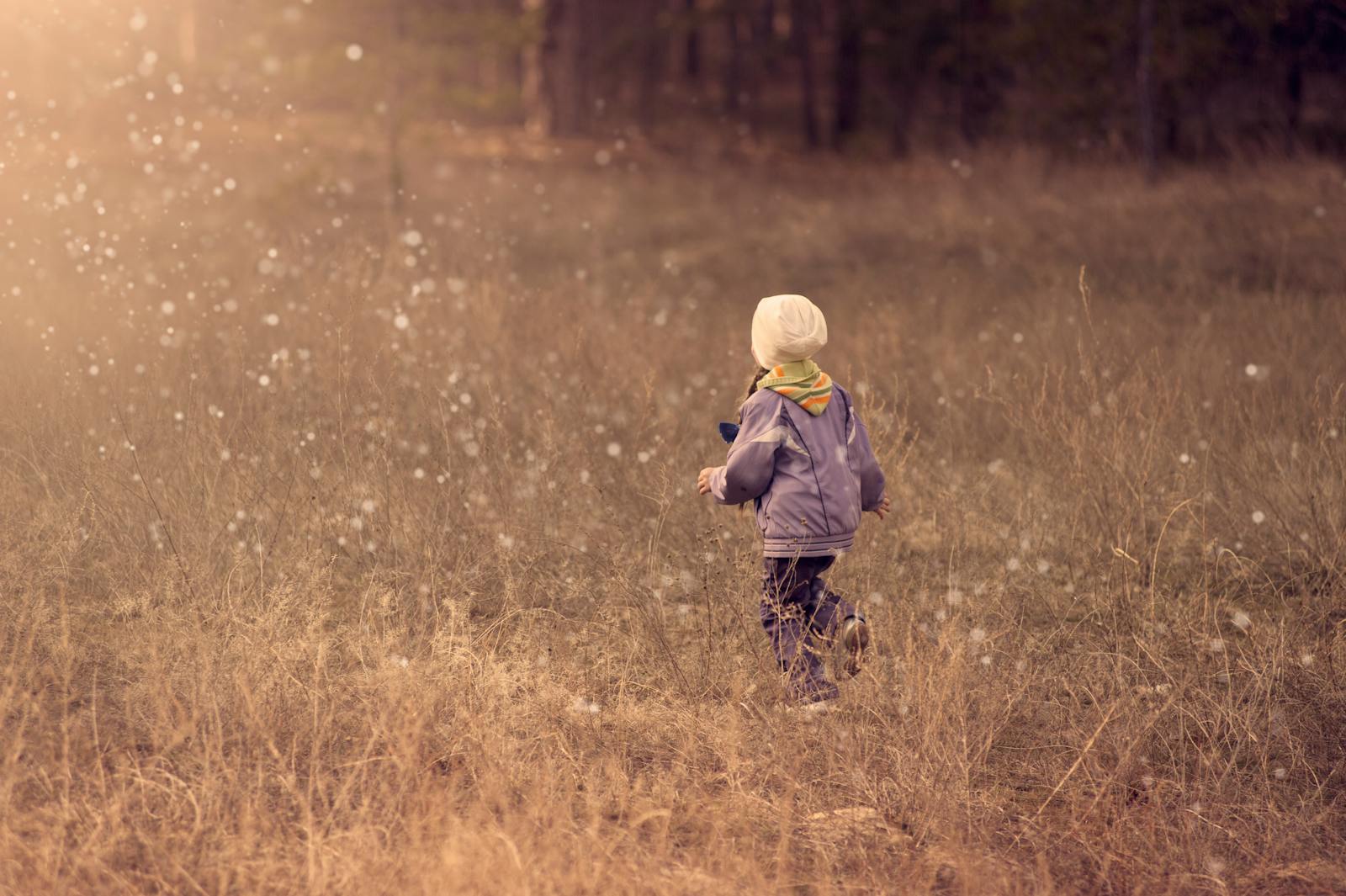 A young child runs through a grassy field during sunset, enjoying the freedom of outdoor play.