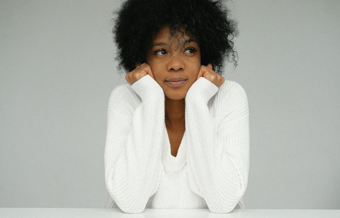 Beautiful portrait of a woman with afro hair in a white sweater, looking pensive.