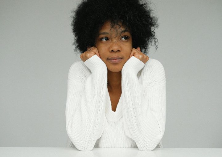 Beautiful portrait of a woman with afro hair in a white sweater, looking pensive.