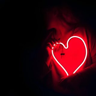 Silhouette of a person with a glowing red neon heart in the dark, symbolizing love.