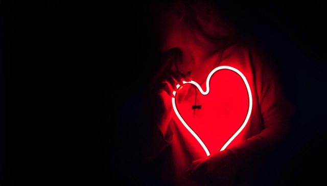 Silhouette of a person with a glowing red neon heart in the dark, symbolizing love.