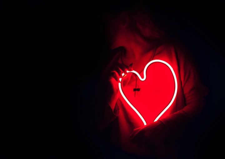 Silhouette of a person with a glowing red neon heart in the dark, symbolizing love.