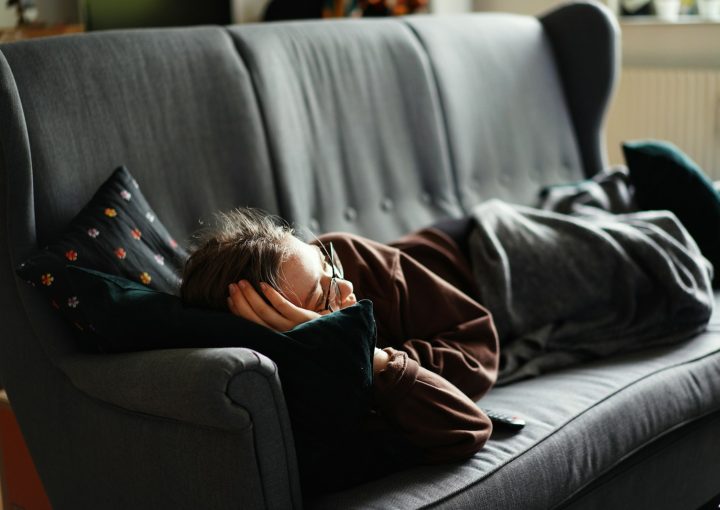 woman in pink jacket lying on gray couch