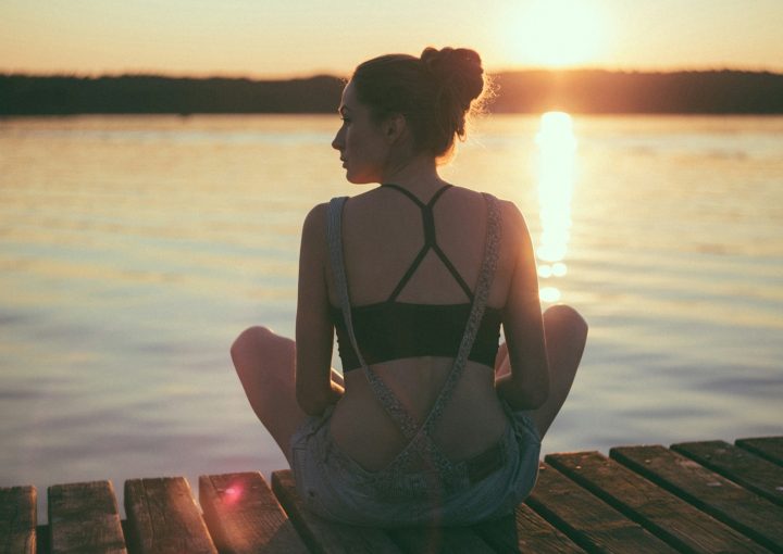woman sitting on brown wooden dock during sunset