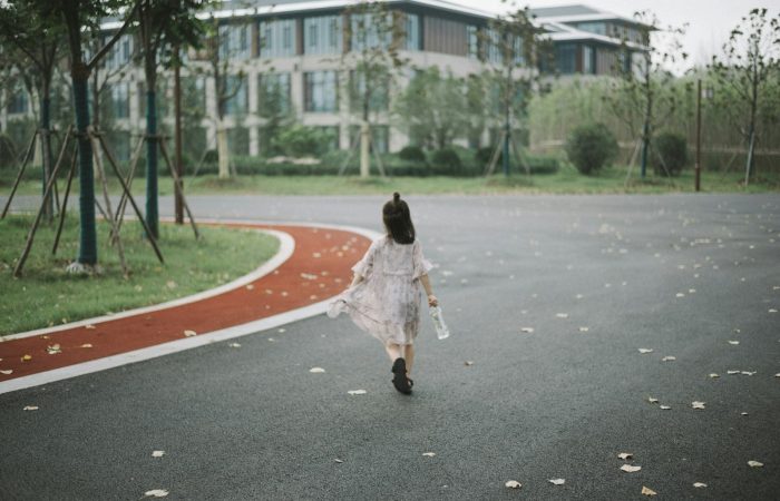 girl holding clear plastic bottle walking on road