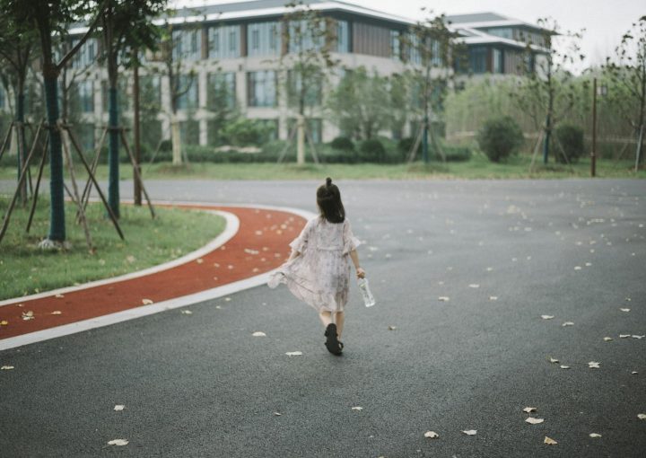 girl holding clear plastic bottle walking on road